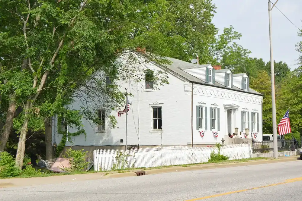 A white brick house with dormer windows and flags beside a street in Columbia, Illinois