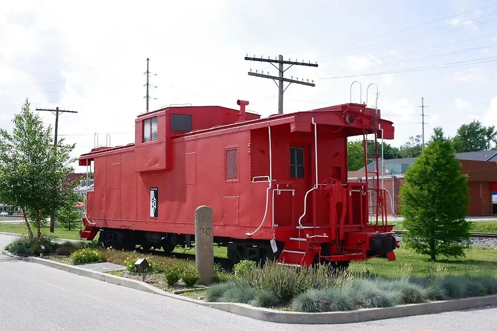 A restored red railroad caboose on display beside a landscaped corner in O'Fallon, Illinois