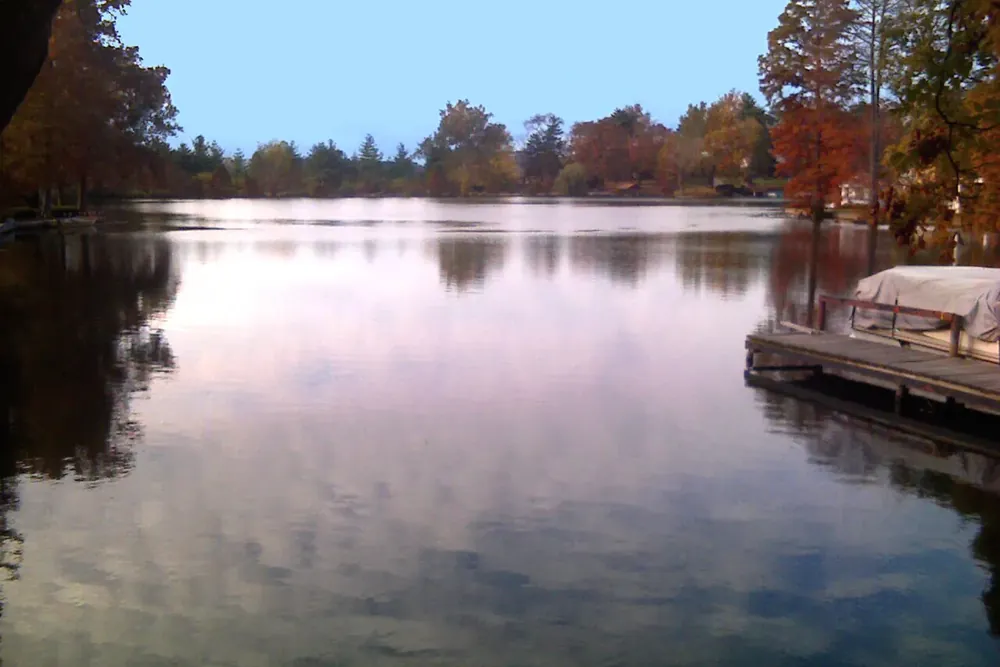 Autumn trees reflected in a calm lake beside a boat dock in Overland, Missouri